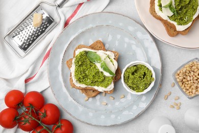 Tasty bruschettas with cream cheese, pesto sauce and fresh basil on light gray table, flat lay