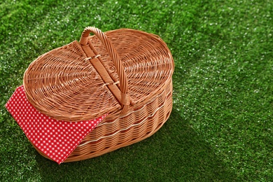 Closed picnic basket with napkin on grass, space for text