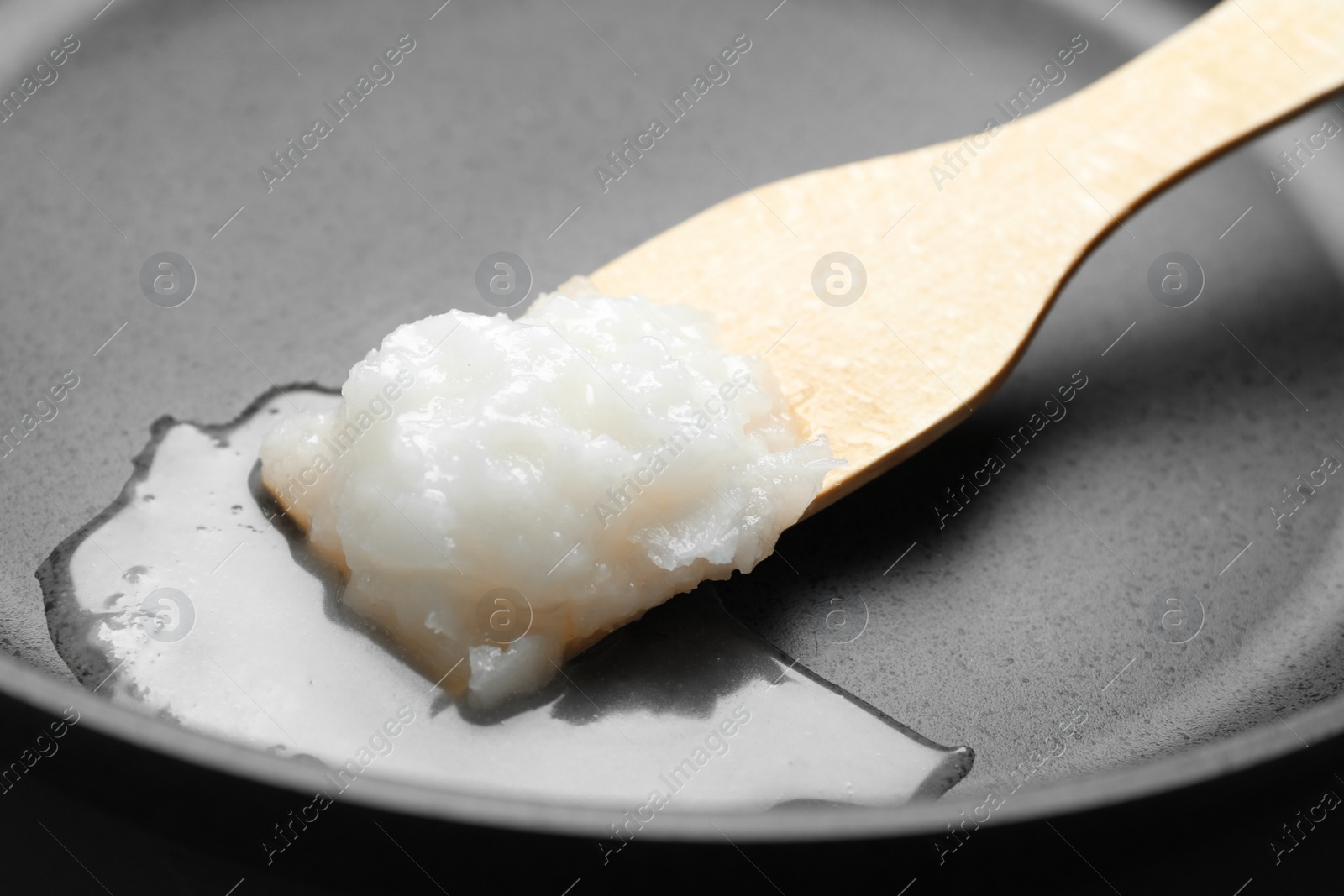 Photo of Frying pan with coconut oil and wooden spatula, closeup. Healthy cooking