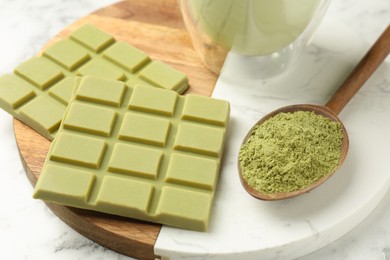 Pieces of tasty matcha chocolate bar and powder in spoon on white table, closeup