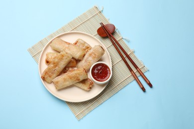Photo of Fried spring rolls and sauce served on light blue table, top view