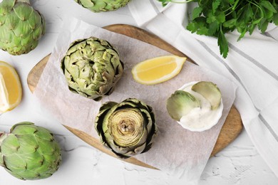 Delicious cooked artichokes with tasty sauce served on white textured table, flat lay