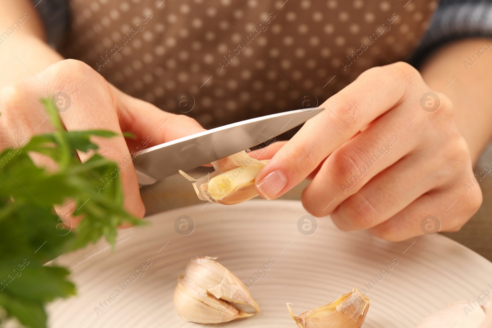 Photo of Woman peeling fresh garlic at table, closeup