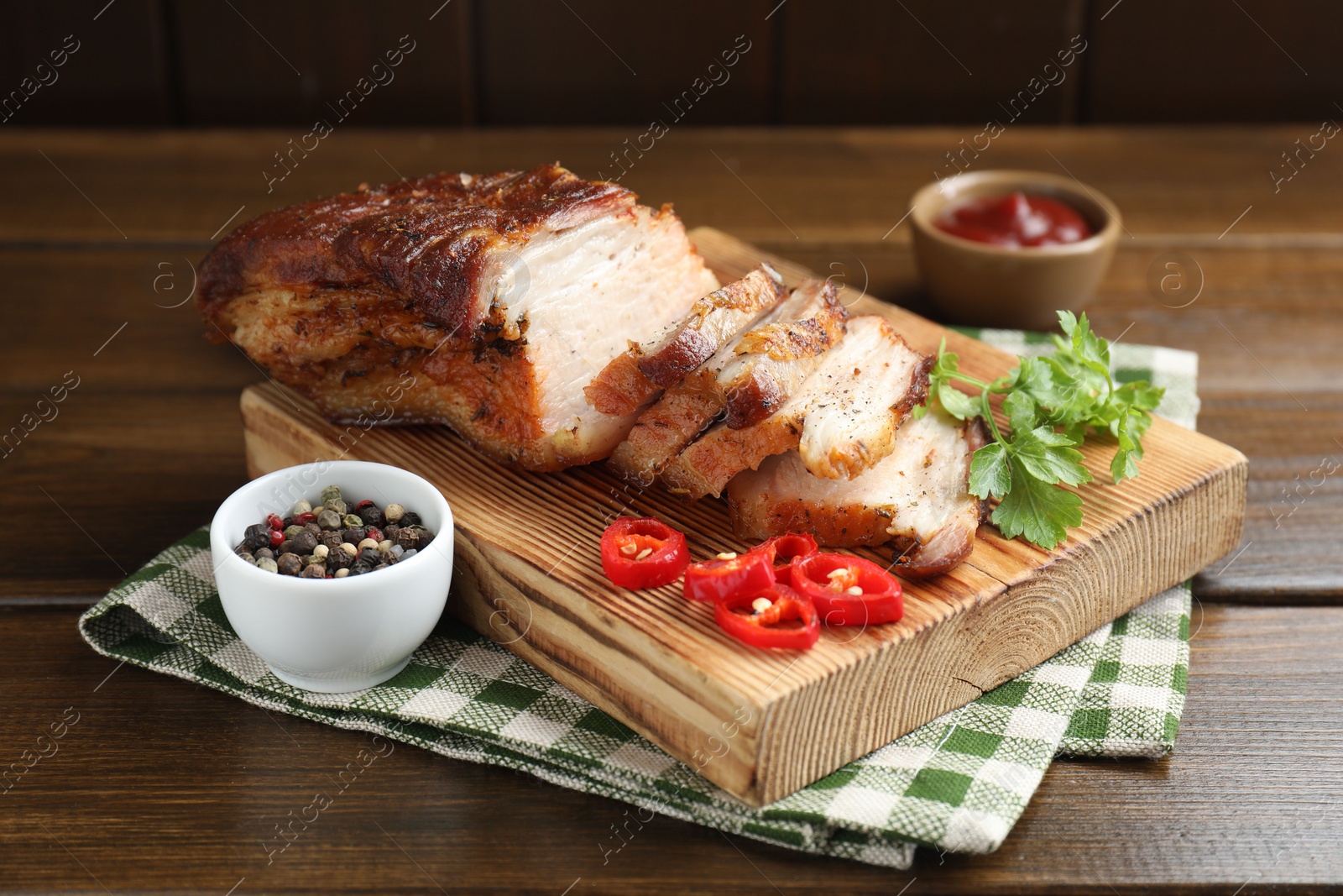 Photo of Pieces of baked pork belly served with sauce, chili pepper and parsley on wooden table