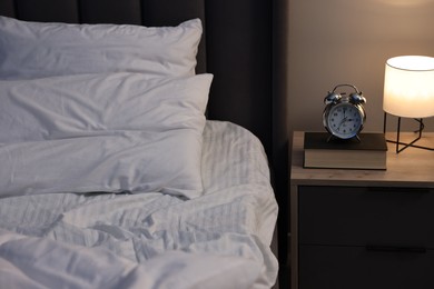 Photo of Nightlight, alarm clock and book on bedside table near bed indoors