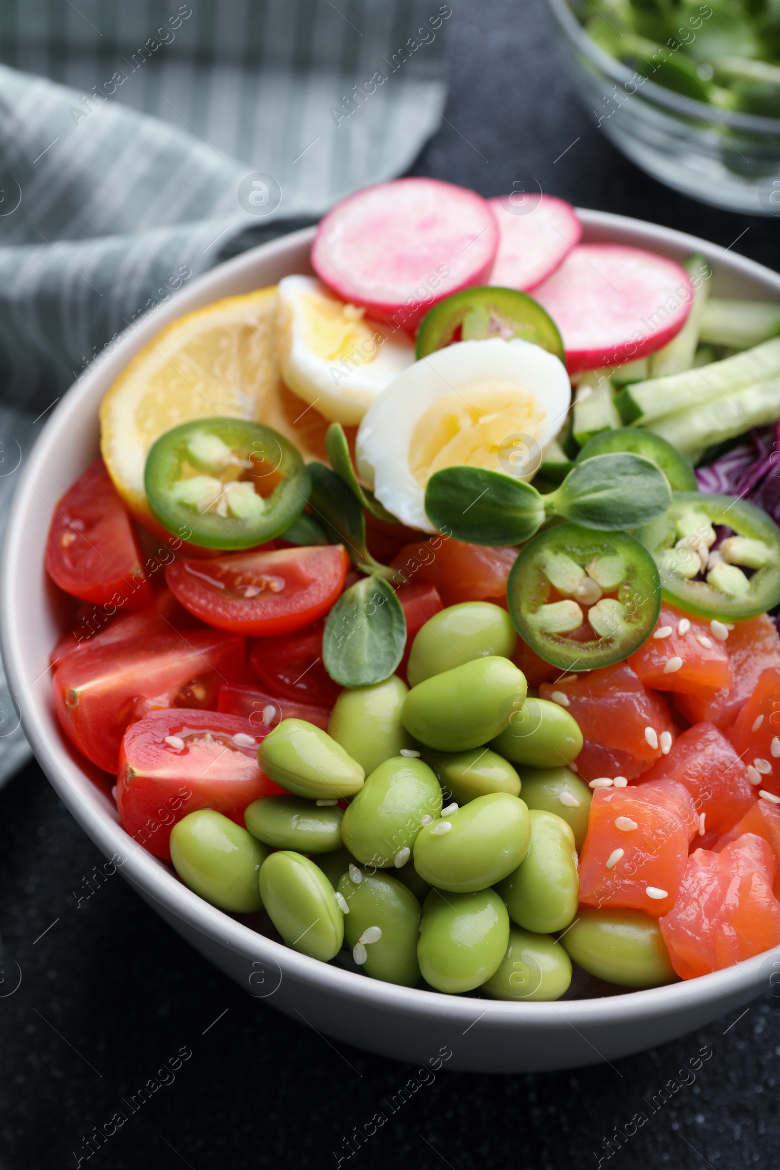 Photo of Poke bowl with salmon, edamame beans and vegetables on black table, closeup