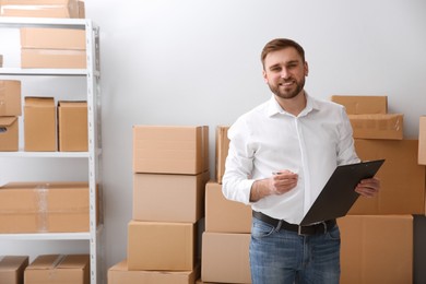 Young businessman with clipboard near cardboard boxes at warehouse