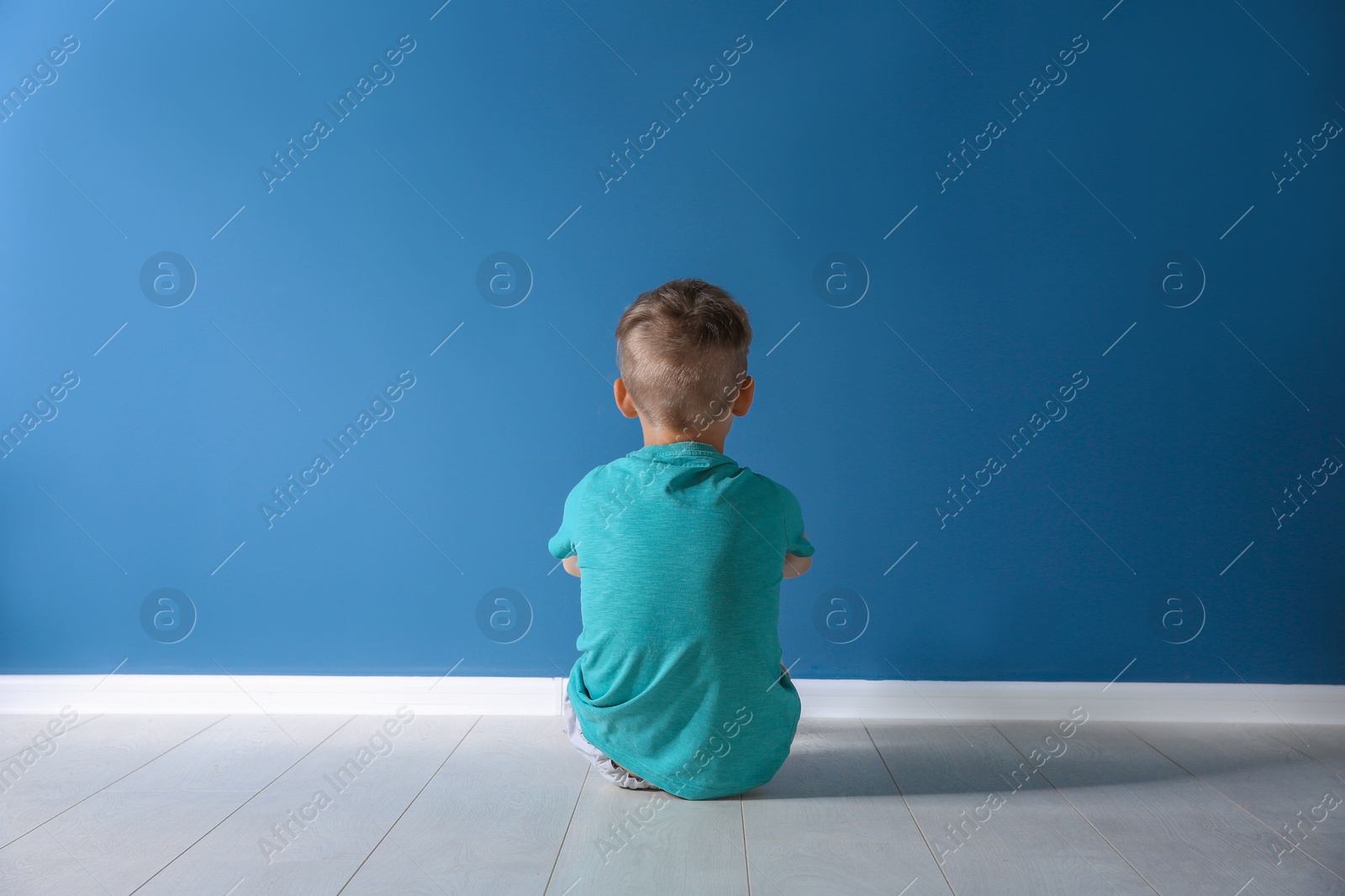 Photo of Little boy sitting on floor near color wall in empty room. Autism concept