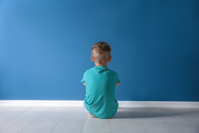 Photo of Little boy sitting on floor near color wall in empty room. Autism concept