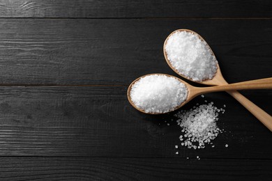 Photo of Organic salt in spoons on black wooden table, top view. Space for text