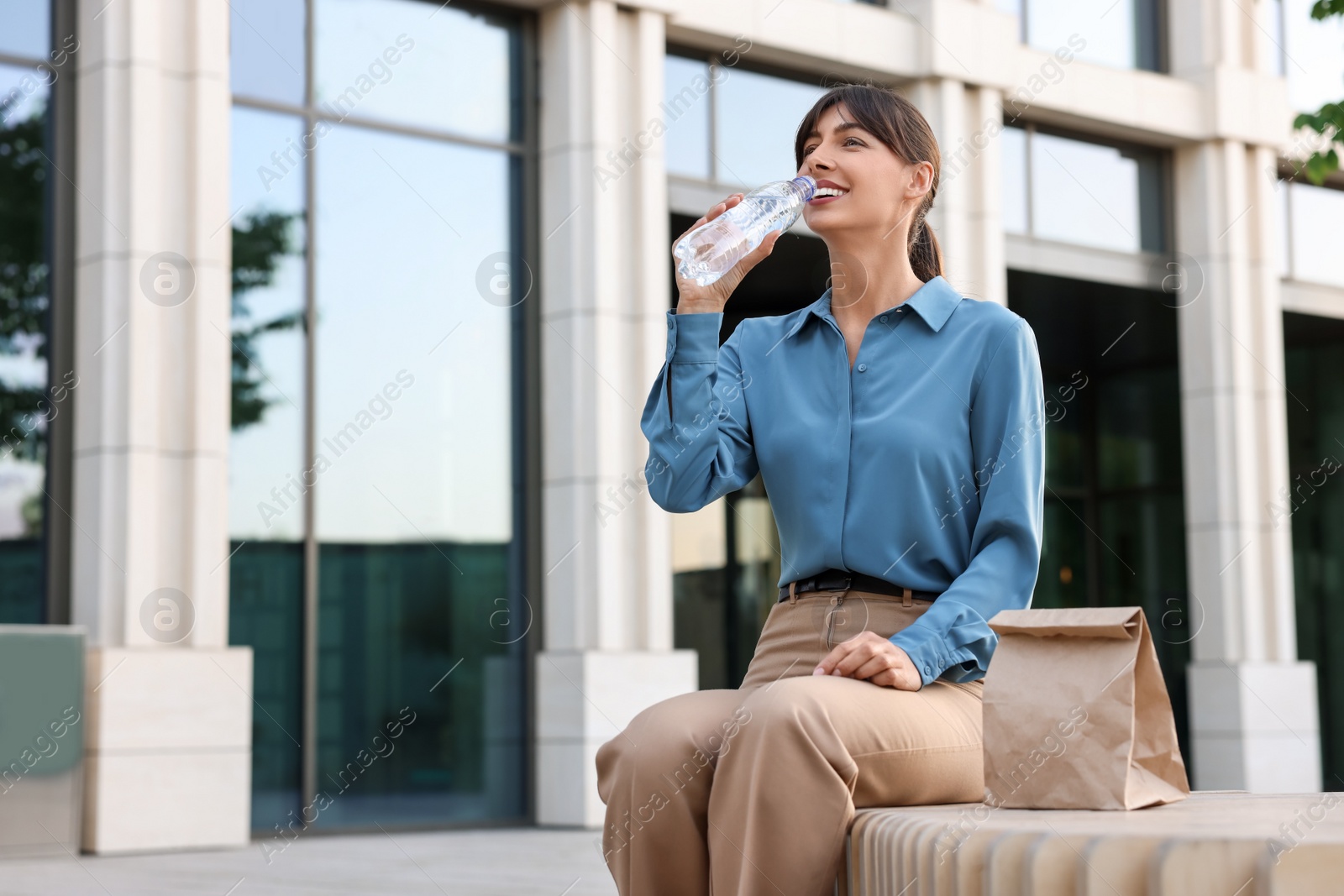 Photo of Lunch time. Businesswoman drinking water from bottle on bench outdoors