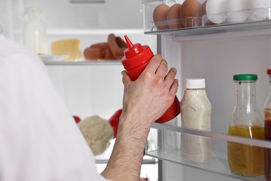 Photo of Man taking ketchup out of refrigerator, closeup