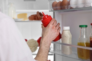 Man taking ketchup out of refrigerator, closeup