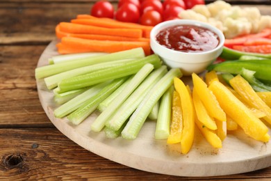 Photo of Board with celery sticks, other vegetables and dip sauce on wooden table, closeup