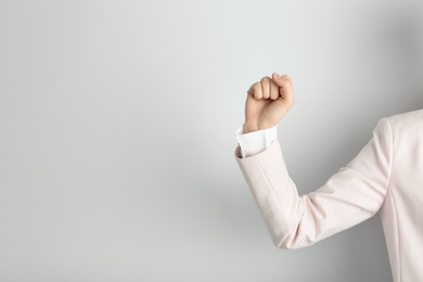 Photo of Young woman showing clenched fist on light background. Space for text