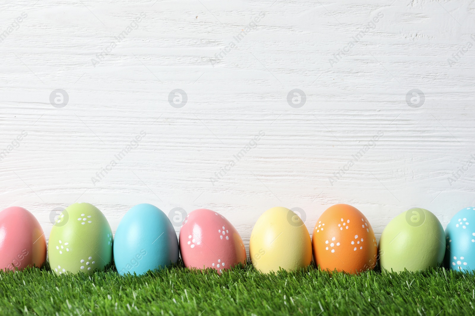 Photo of Colorful painted Easter eggs on green grass against wooden background, space for text