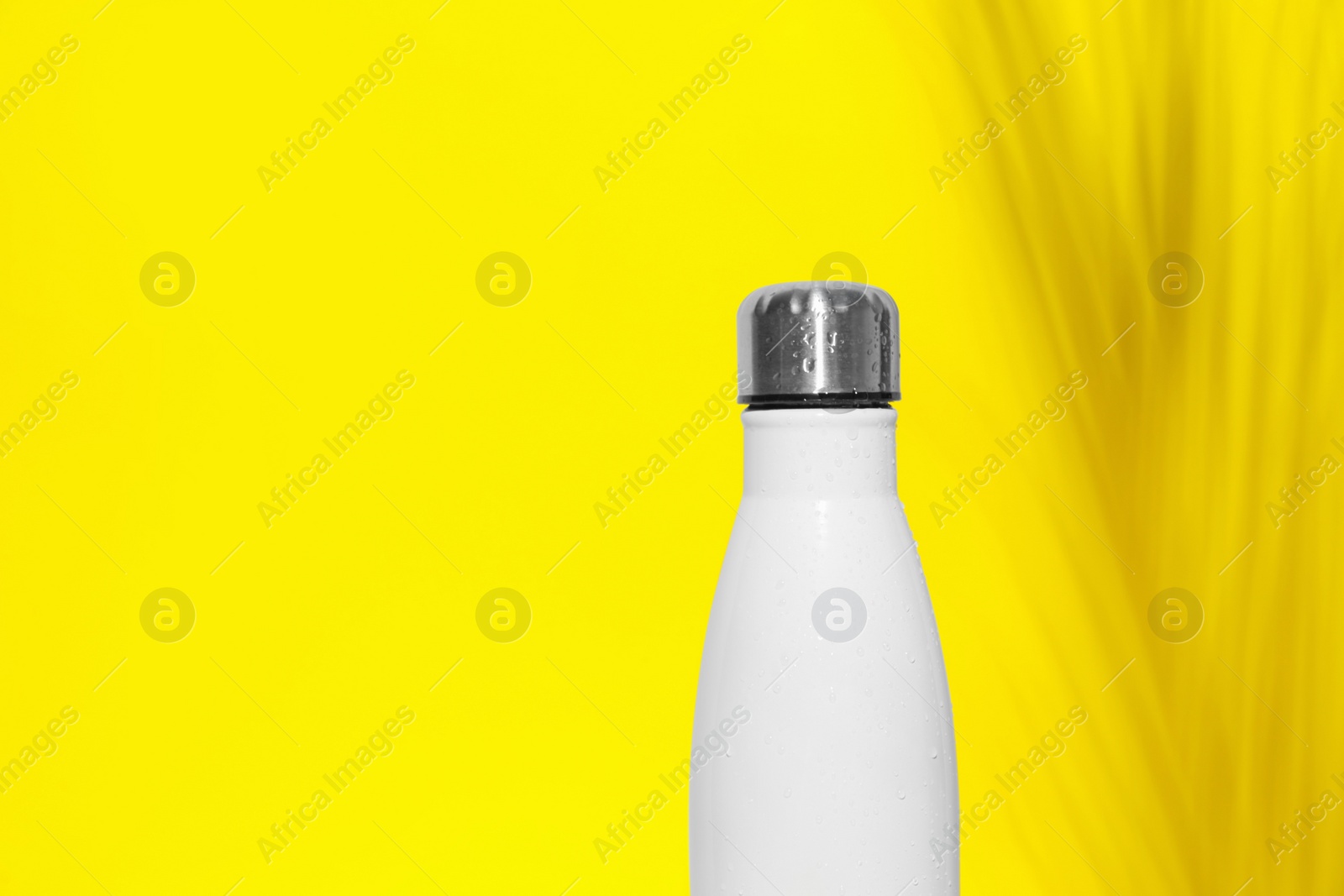 Photo of Stylish white thermo bottle with water drops on yellow background, space for text