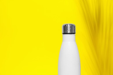 Stylish white thermo bottle with water drops on yellow background, space for text