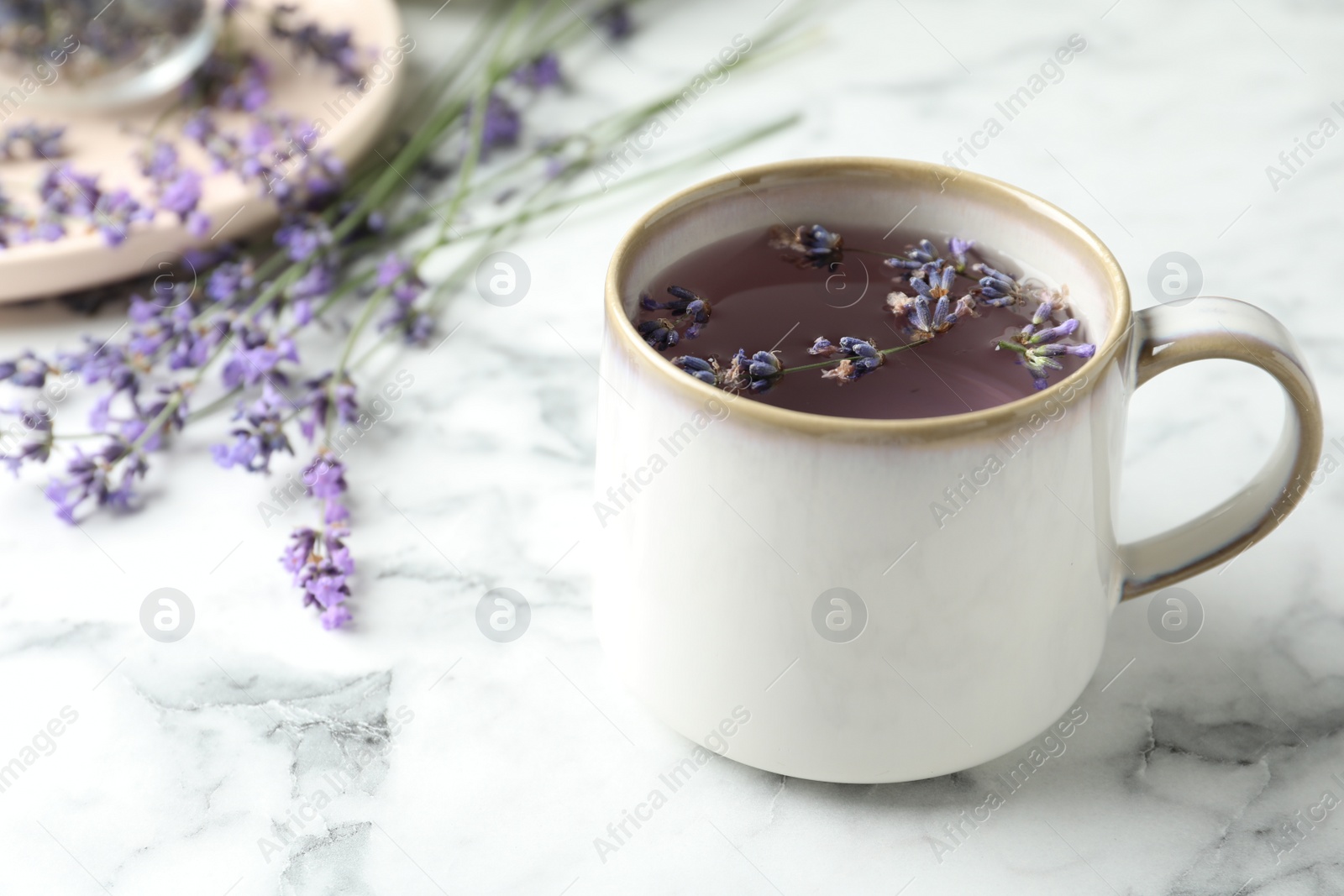 Photo of Fresh delicious tea with lavender and beautiful flowers on white marble table