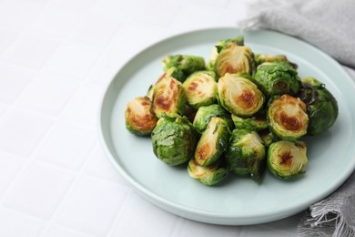 Photo of Delicious roasted Brussels sprouts on white tiled table, space for text