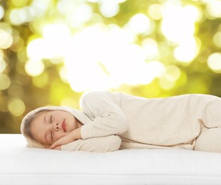 Image of Little girl sleeping on comfortable mattress against blurred green background, bokeh effect. Sleep well - stay healthy