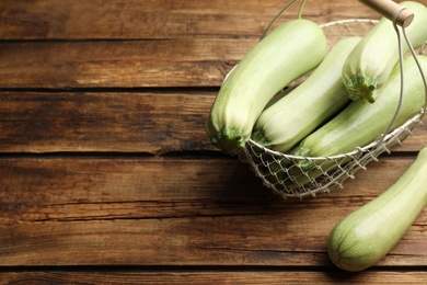 Photo of Basket with ripe zucchinis on wooden table, above view. Space for text