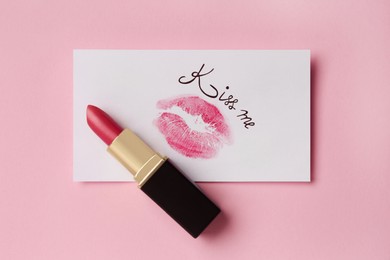 Photo of Paper card with lip print, phrase Kiss Me and lipstick on pink background, top view