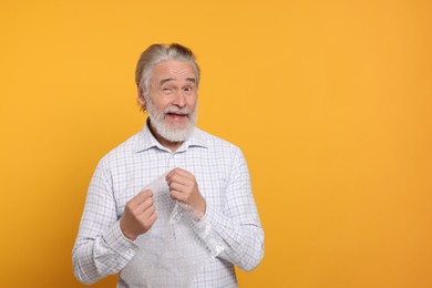 Emotional senior man popping bubble wrap on yellow background, space for text. Stress relief