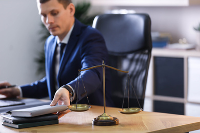 Photo of Male lawyer working at table in office, focus on scales of justice