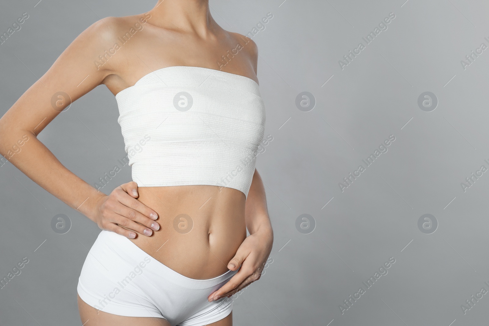 Photo of Bandaged young woman after plastic surgery operation on grey background, closeup. Space for text