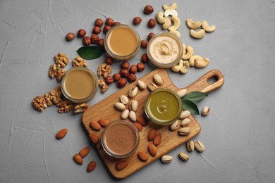 Jars with butters made of different nuts and ingredients on grey table, flat lay