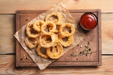 Photo of Homemade crunchy fried onion rings and sauce on wooden background, top view