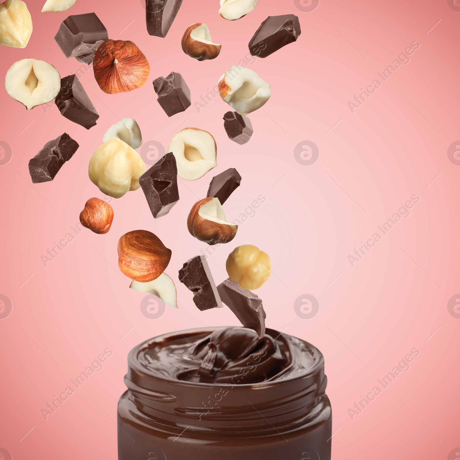 Image of Making yummy chocolate paste. Hazelnuts and pieces of chocolate falling into jar on pale red background