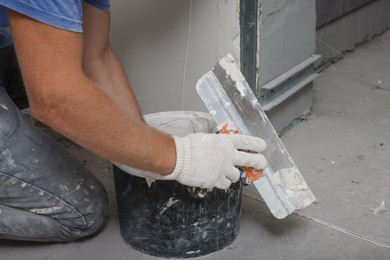 Photo of Worker plastering wall with putty knife indoors, closeup