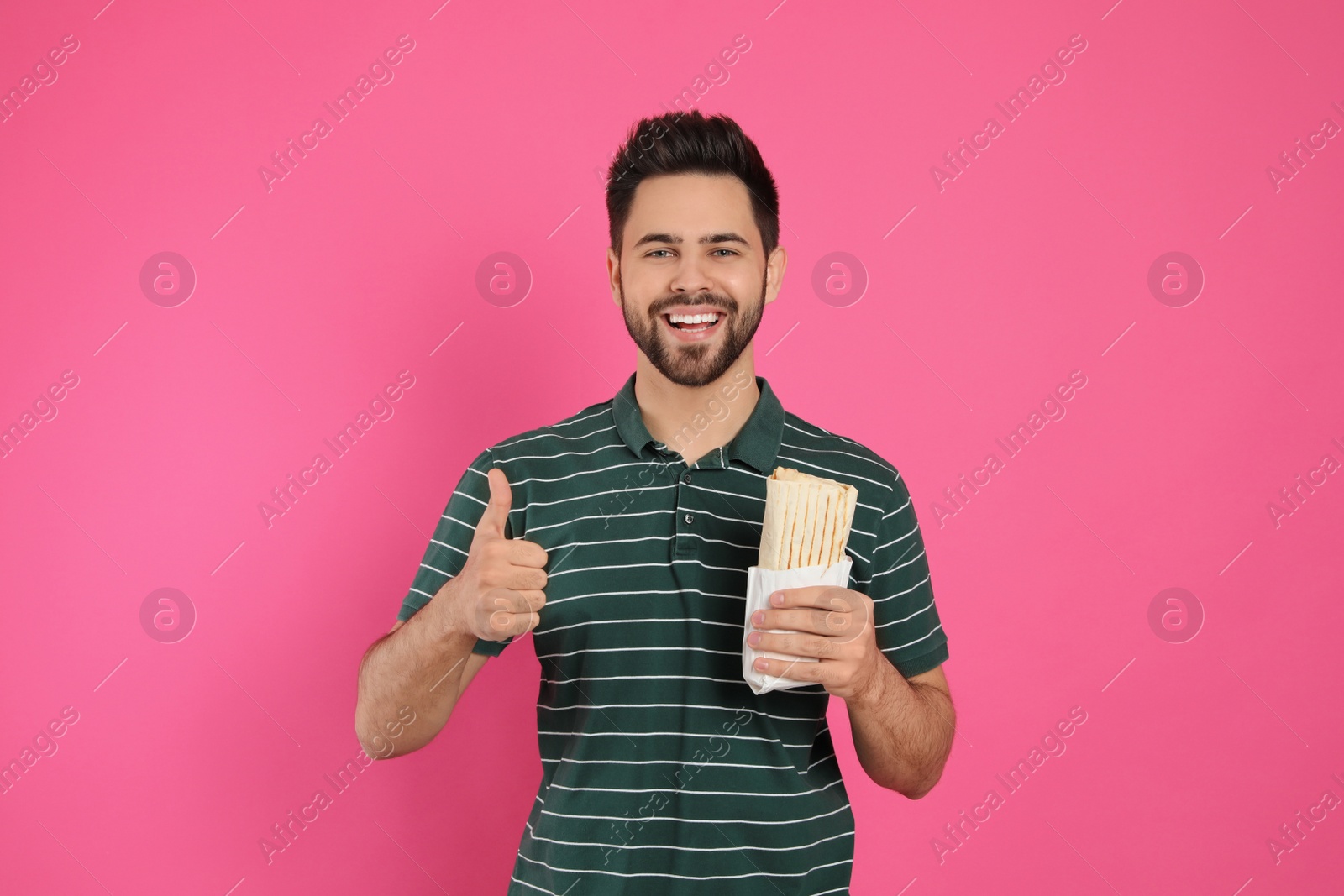 Photo of Happy young man with tasty shawarma showing thumb up on pink background