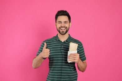 Photo of Happy young man with tasty shawarma showing thumb up on pink background