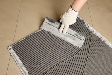 Photo of Worker spreading concrete over ceramic tile with spatula on floor, closeup. Space for text