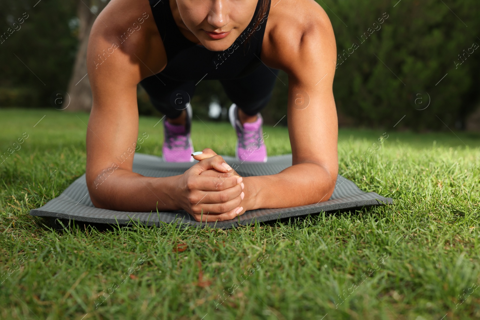 Photo of Young woman doing plank exercise on grass in park, closeup
