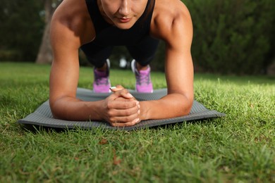 Young woman doing plank exercise on grass in park, closeup