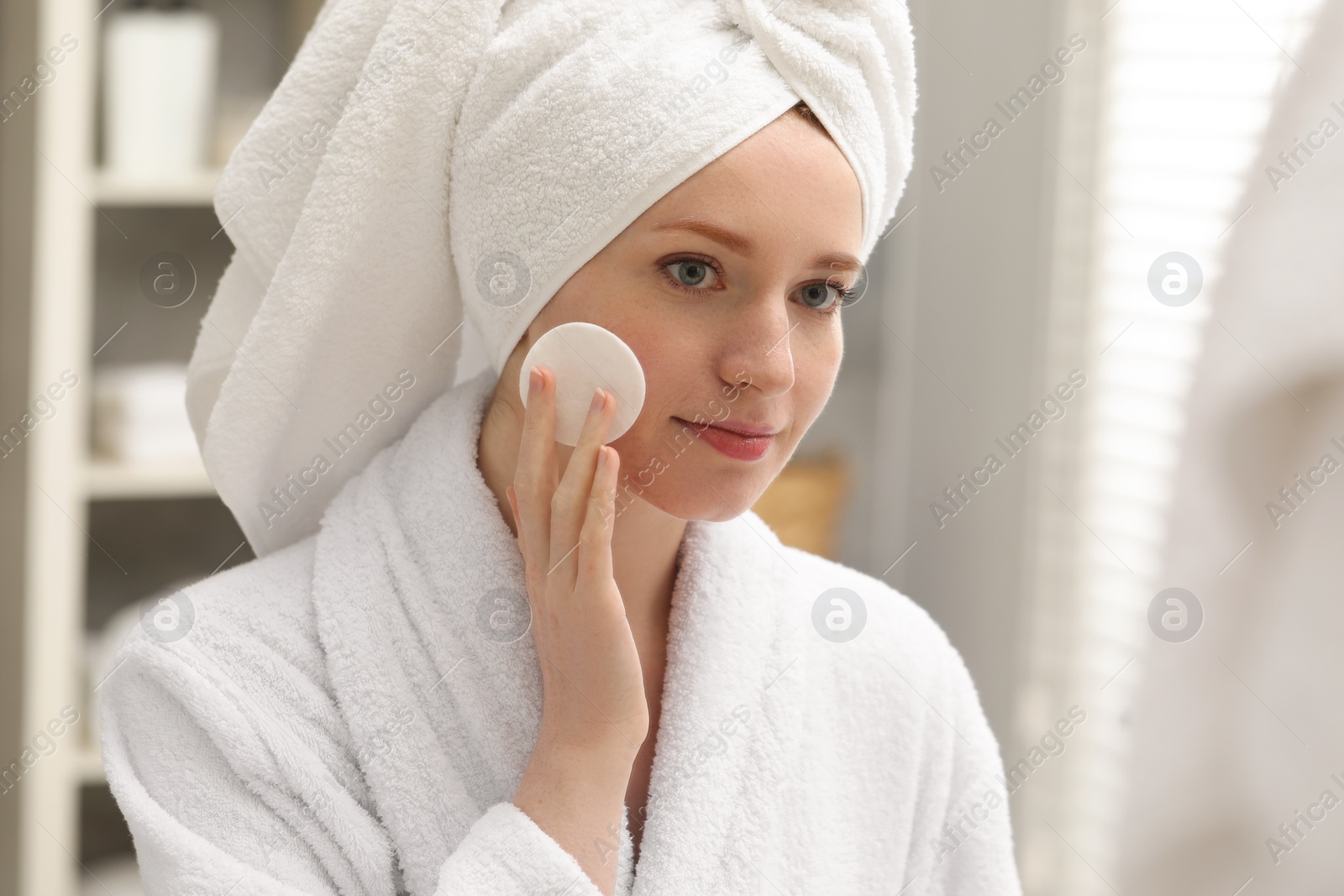 Photo of Beautiful woman with freckles wiping face in bathroom