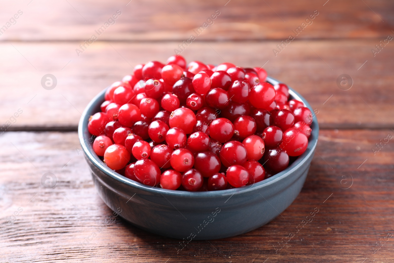 Photo of Fresh ripe cranberries in bowl on wooden table, closeup