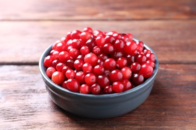 Photo of Fresh ripe cranberries in bowl on wooden table, closeup