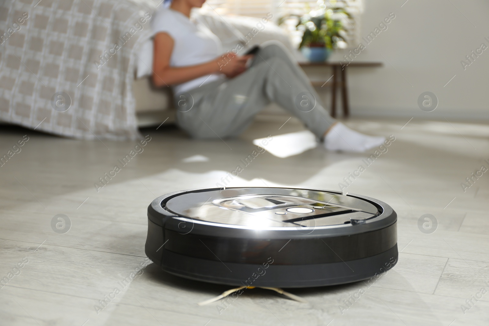 Photo of Modern robotic vacuum cleaner and blurred woman resting on background