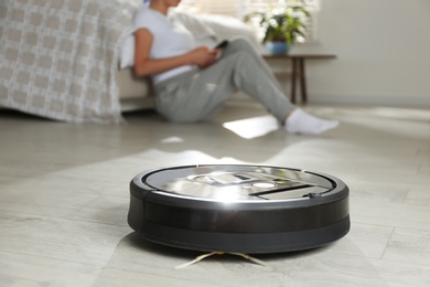 Modern robotic vacuum cleaner and blurred woman resting on background