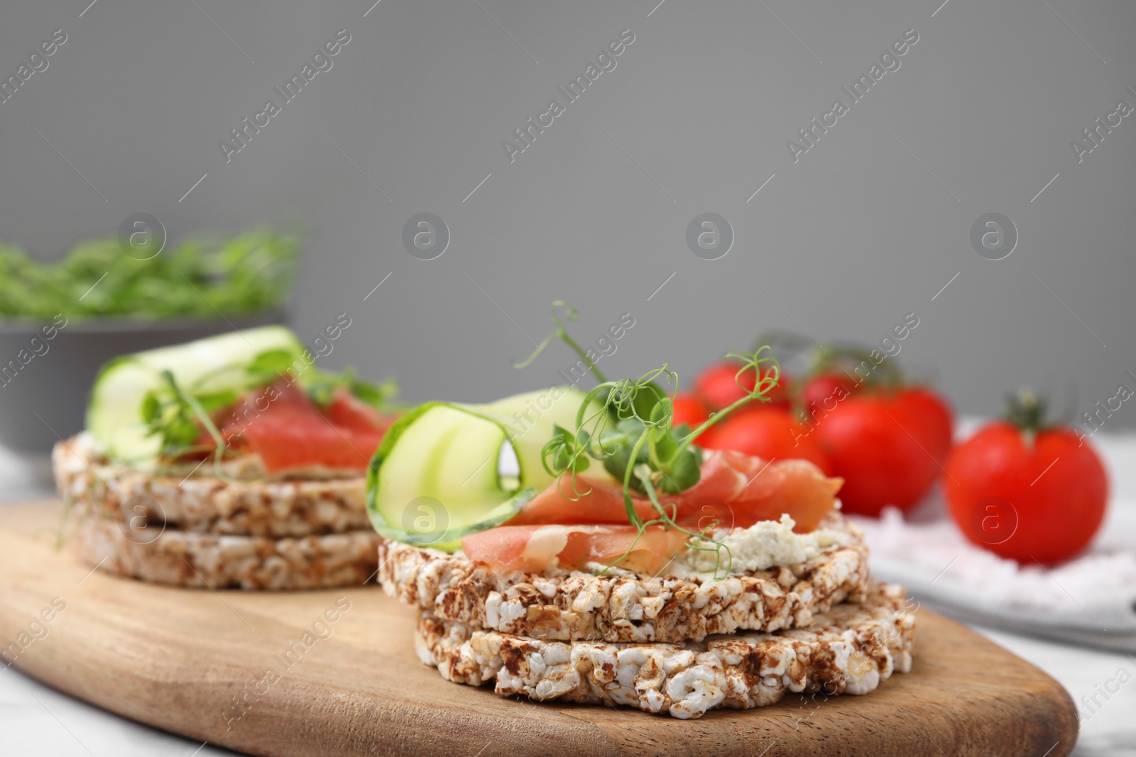 Photo of Crunchy buckwheat cakes with cream cheese, prosciutto and cucumber slices on wooden board, closeup