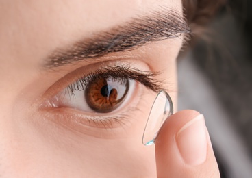 Photo of Young woman putting contact lens in her eye, closeup