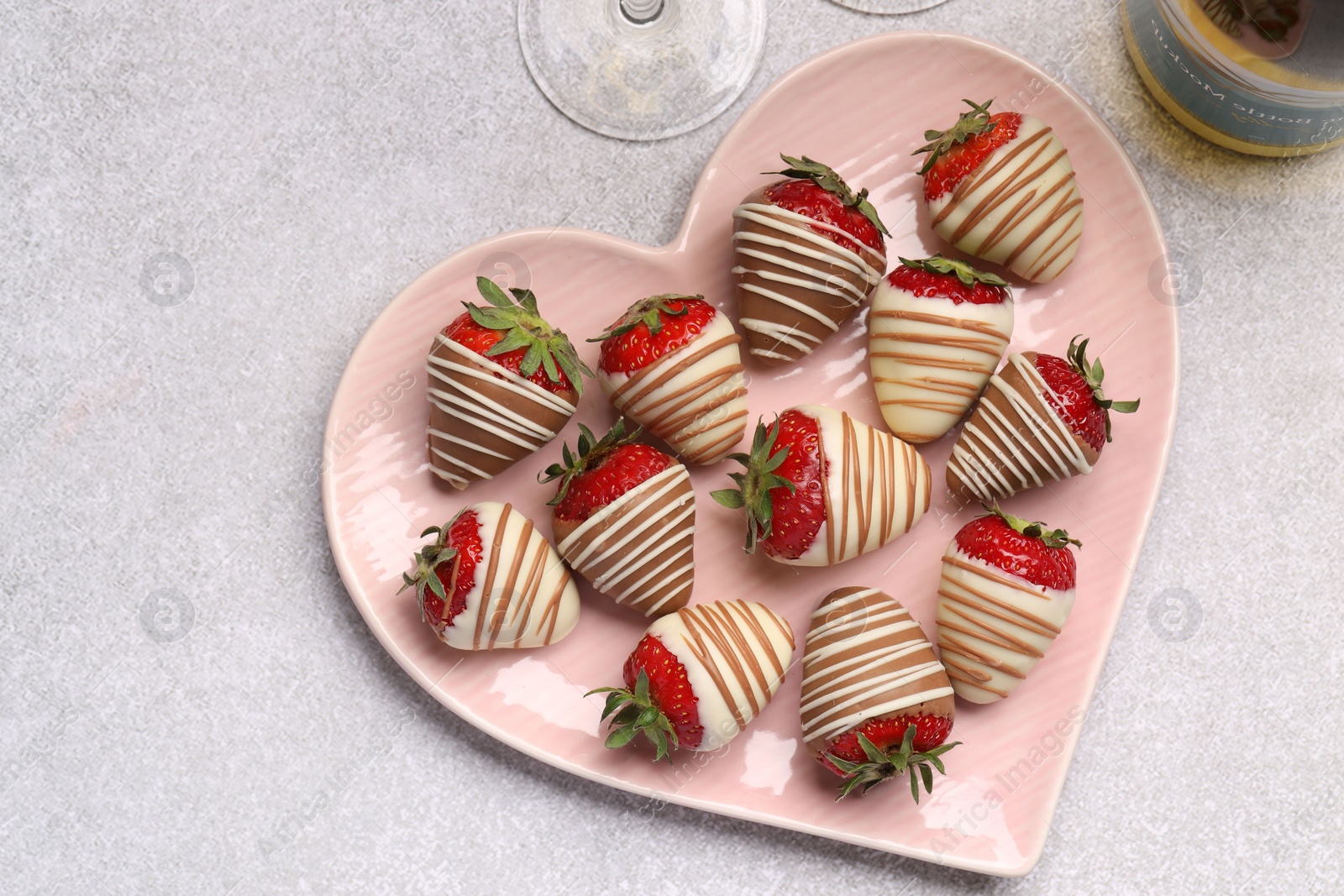 Photo of Heart shaped plate with delicious chocolate covered strawberries and sparkling wine on light table, flat lay