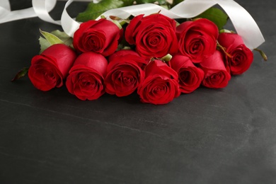 Photo of Beautiful red roses with white ribbon on dark table, space for text. St. Valentine's day celebration