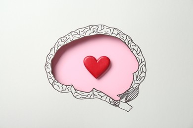 Photo of Emotional thinking. Red heart on pink background, top view through paper with brain shaped hole and drawing