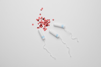 Photo of Tampons and red sequins on white background, flat lay. Menstrual hygiene product
